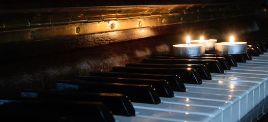 There is a burning candle on the piano keys. Concept - an evening of memories, performance of music.