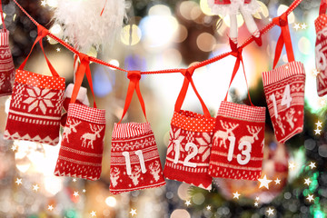 Small bags as Advent calendar with Sweets surprises hanging on a ribbon against lights blurred...