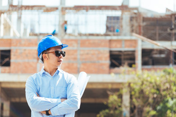 Civli engineer with blue safety helmet and sunglasses holding blueprint or drawing at construction site