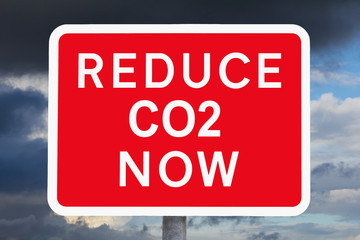 Climate change concept: REDUCE CO2 NOW text on red and white warning sign in front of dark sky.