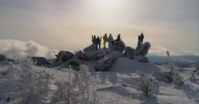 Tourists stand on top of the winter mountain and looking at the clouds below, back view. Aerial view. Epic free ride scene. a group of skiers and snowboarders on top of a mountain. camera in motion