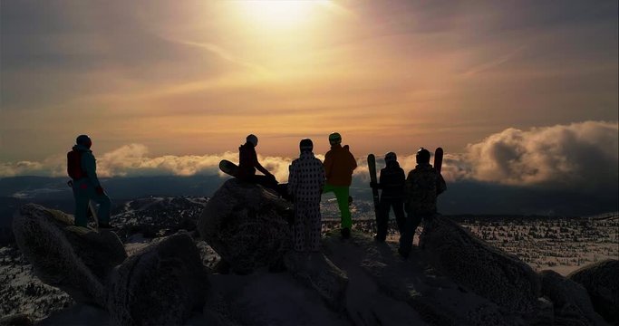 Aerial - friends riders stand on top of the winter mountain and looking at the clouds below, back view. Epic free ride scene. a group of skiers and snowboarders on top of a mountain. camera in motion