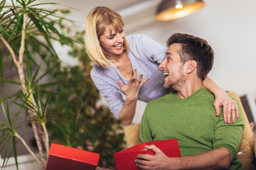 Naklejka premium Happy man receiving a present from his girlfriend while sitting on the sofa