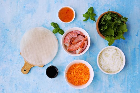 Ingredients for cooking spring rolls: sheets of rice paper, rice noodles, grated carrots, shrimps, salad mixture, soy sauce, chili sauce, basil. Top view. Vietnamese cuisine.