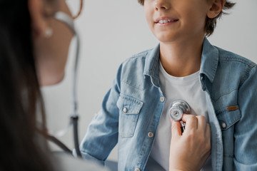 Cropped image of female pediatrician doing a medical checkup with stethoscope of young boy - obrazy, fototapety, plakaty