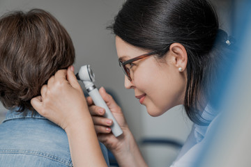 Close up of doctor examining boy's ear with otoscope in medical cabinet