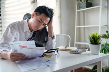 Stressed young asian businessman holding so many expenses bills such as electricity bill,.water bill,internet bill,cell phone bill and credit card bill in his hand no money to pay debt