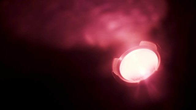 Close up of red spotlight blinking in complete darkness. Action. Red soffit shimmering in the dark room, being turned on isolated on black background.