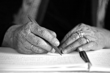 Close up of elderly woman hands writing; life-long learning concept, B&W.