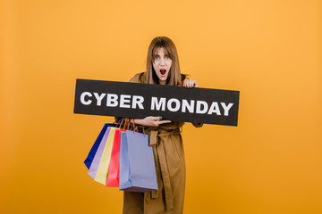 surprised excited girl in autumn coat and cyber monday sign and colorful shopping bags isolated over yellow