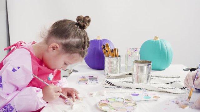 Step by step. Little girl painting mermaid tails and seashells with acrylic paint to decorate Halloween pumpkins.