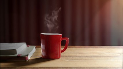 Focus on hot coffee in red cup with steam and white books on wooden table with morning warm light shining through the window in living room at home, morning coffee concept