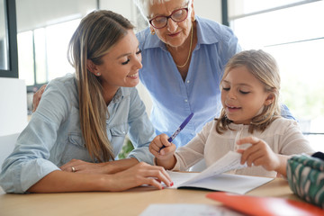 Little girl doing homework, mom and grandma watching her