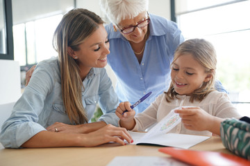 Fototapeta premium Little girl doing homework, mom and grandma watching her