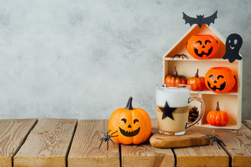 Halloween holiday concept with latte macchiato coffee cup and jack o lantern glitter pumpkin decor...