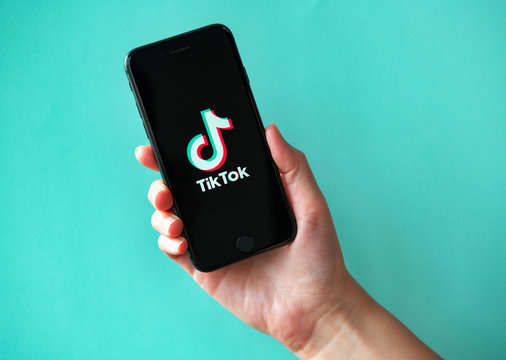 Kyiv, Ukraine - October 1, 2019: Studio shot of hand holding Apple iPhone 8 with TikTok logotype on a screen. Isolated on a vibrant cyan paper background.