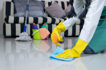 Asian woman in green overalls and yellow, rubber gloves dusting a floor.