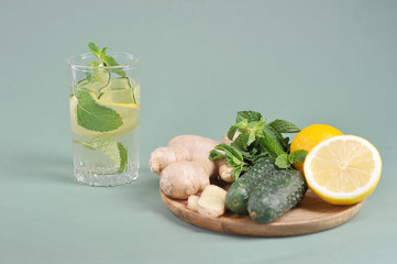 Fresh, detox drink water sassi. Ingredients for making a sassi drink: lemon, cucumbers, ginger root, mint on a round wooden tray. Light background. 