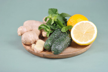 Ingredients for making a fresh, detox sassi drink. Lemon, cucumbers, ginger root, mint on a round wooden tray. Light background. Close-up.