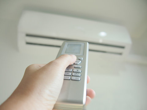 Man using hand remote control adjusting and regulating temperature the air conditioner for energy savings