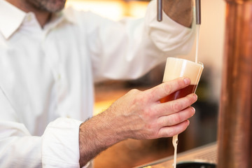Pouring beer for client. Bartender pouring beer while standing at the bar counter.