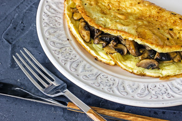 Omelet mushrooms on a white plate on a dark table, next to cutlery. A wholesome breakfast for keto and paleo diets. Ketogenic breakfast. Omelette mushrooms