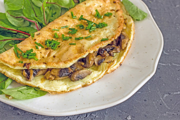 Omelet with mushrooms and herbs on a white plate on a dark background. Delicious homemade breakfast for keto diets.  The concept of a keto diet, high-grade nutrition, keto breakfast.