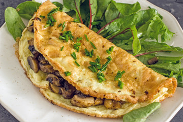 Omelet with mushrooms and herbs on a white plate on a dark background. Delicious homemade breakfast for keto diets.  The concept of a keto diet, high-grade nutrition, keto breakfast.