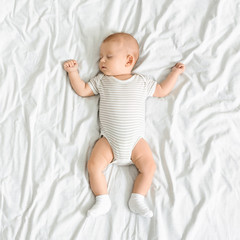 Adorable newborn baby napping in bed with arms up