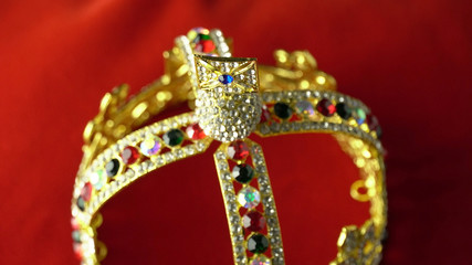 Gold diamond crown or decorative pageant accessory close up focus on the top. On the red royal color surface.