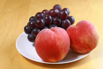 Naklejka na ściany i meble Peaches and black grapes on the white plate