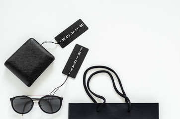 Flat lay of men stuffs - black wallet, sunglasses, price tags and shopping bag on white background for Black Friday sale concept.