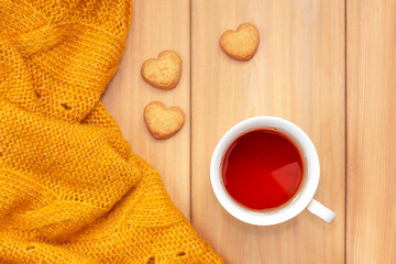 Cup of tea, sweet cookies in shape of heart and plaid on wooden background. Cold weekend at cozy home. Fall season. Cute autumn still life. Autumnal mood concept.