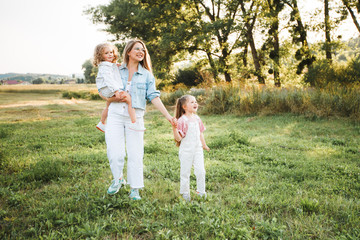 Blonde mother with two cute daughters are walking and having fun outdoors. Stylish, casual clothes.