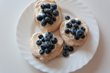 Pavlov cakes with cream and fresh blueberries on a white plate