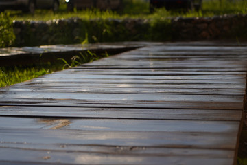 A wet wooden sidewalk and green grass on the background
