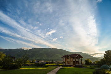 Green grass with cottage and touristic tents, mountains on the background