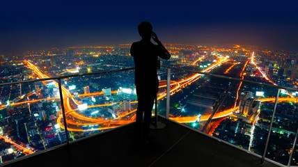 Businessman standing using smart phone on open roof top balcony watching city night view.Business...