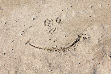 a smile drawn with a stick in the sand on a beach