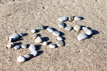 Fototapeta na wymiar the letters SOS written on sand on a beach with stones with space on teh right for copy