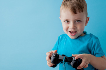Little kid boy 2-3 years old wearing blue clothes hold in hand joystick for gameson blue background children studio portrait. People childhood lifestyle concept. Mock up copy space
