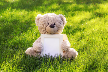 Mockup. Soft beige teddy bear toy holding white clean mock up frame with copy space sitting on...