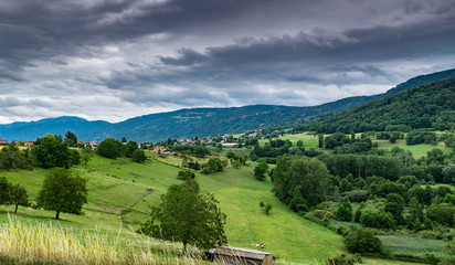 View of the mountain landscape,green pastures, trees, forests on the slopes of hills and farmhouses with a cloudy sky in the background.Brens,Haute-Savoie in France.