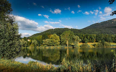 View of the lake, forest, mountains and blue sky with clouds,focus in the center of the picture.Lake Machilly, Le Signal des Voirons mountain peak,Haute-Savoie in France.