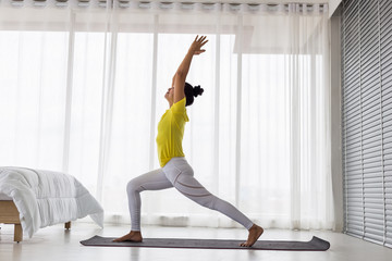 young Asian lady wearing yellow t shirt doing exercise Yoga pose in the bedroom in the morning.