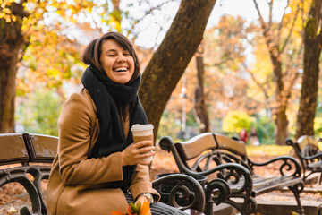 Fototapeta na wymiar woman sitting on the bench at autumn city park drinking coffee