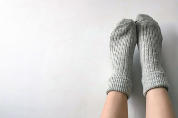 Women wearing grey knitted cozy socks on gray background. Сopyspace for text 