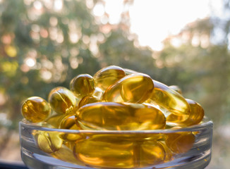 Fish oil capsules in a transparent plate. A lot of vitamin omega-3 against the background of nature and the park. Close up, high resolution product. Metabolism in the body. The body of calcium. 