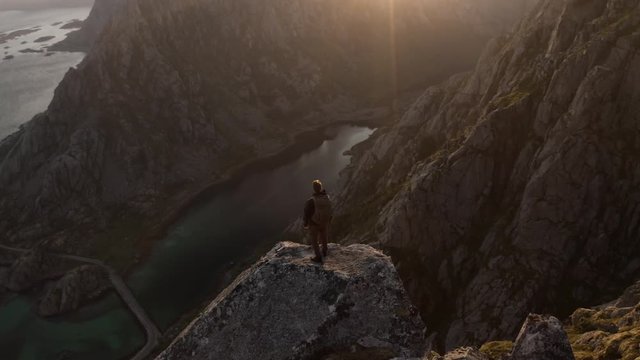 Midnight sun in Lofoten, Norway. Man standing on an epic rock.