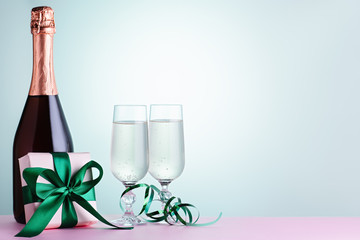 Two glasses of sparkling wine, champagne bottle and gift box in green and mint colors, copy space